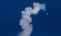 A small light againsta blue sky with a large plume of smoke trailing behind it