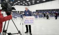 A man standing in front of a TV camera holding a sign that says "Fair Maps. Make them earn our vote."