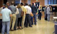 A long line of people waiting to vote, a few people standing at voting booths and a woman walking back down the line.
