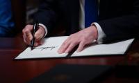 A man's hand signing a piece of paper on a desk