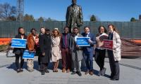 A group of people standing in front of a statue holding signs that say "Maryland needs a voting rights act"