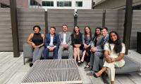 A group of people sitting on an outdoor couch on a roof deck.