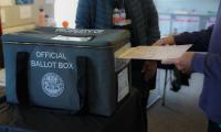 A person inserting a ballot into a box labeled "Official Ballot Box"