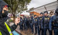 A man wearing a mask films a line of officers with his phone.