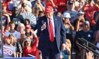 Donald Trump wearing red tie and usa hat giving thumbs up to a crowd of people.