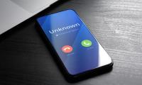 A smartphone on a desk with the words "Unknown, Potential Spam" on the screen and green and red buttons to decline or accept the call.