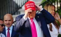 Donald Trump putting on a red had with the words "Make America Great Again" on it.
