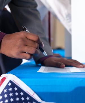 Man's hands writing on ballot in voting booth