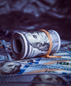 A roll of $100 bills on top of a pile of other $100 bills
