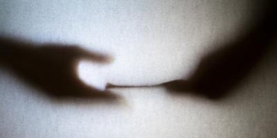 Two hands seen through frosted glass. One is passing a stack of what looks like money to another.