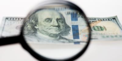A magnifying glass hovering over a $100 bill.