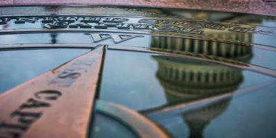 The dome of the U.S. Capitol Building reflected in a puddle on top of a compass rose