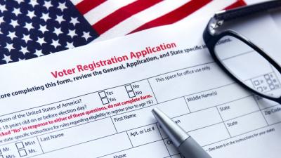 A voter registration form with a pen and glasses on top of an American flag
