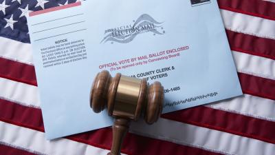 A gavel lies on top of a mail voting envelope on top of an American flag.