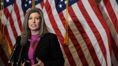 Joni Ernst speaking at a podium in front of an American flag