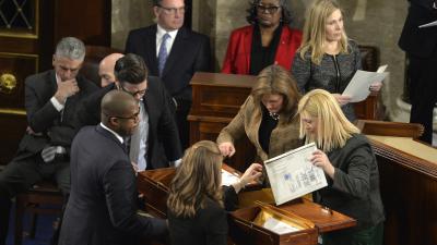 A group of people in suits, gathered around boxes, unsealing envelopes.