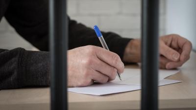 A man's hand holding a pen and writing behind bars