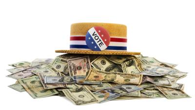 A straw hat with a red white and blue ribbon and a "Vote" button on it sitting on top of a pile of money