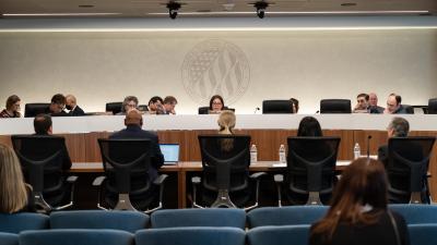 FEC commissioners sit behind a desk facing five people seated in chairs at a desk in front of them.