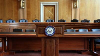 A podium with a microphone with the Senate seal on the front in front of two rows of chairs behind desks
