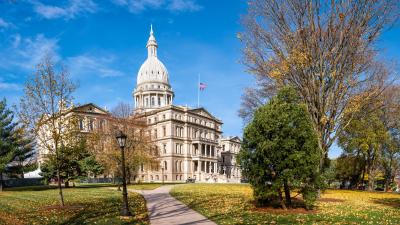The Michigan state capitol building surrounded by trees on a sunny fall day