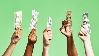 A row of people's hands holding up money against a green background