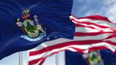 The state flag of Maine waiving in the breeze with an American flag behind it