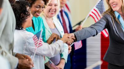 A woman shakes hands with a group of other women holding American flags