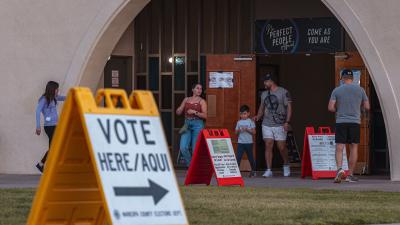 People exiting the doors of a building with a "Vote Here" sign in the foreground.