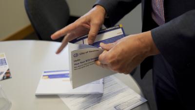 A man's hands opening an envelope that says "City of Seattle. Hello, your four $25 Democracy Vouchers..."