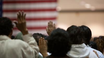 People raise their hands while standing in front of an American flag on the wall