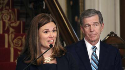 A woman speaking at a podium with a man standing behind her