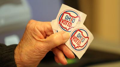 A person's hand holding two stickers that say "Ohio Voted"