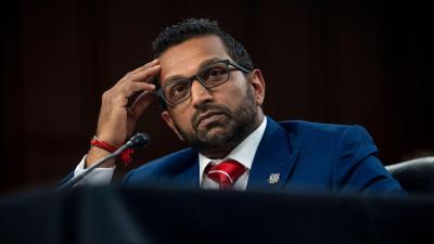 Kash Patel sitting at a desk with his hand raised to his forehead