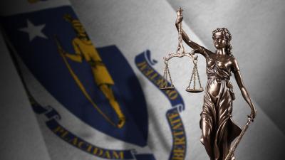 A statue of Lady Justice in front of the Massachusetts state flag