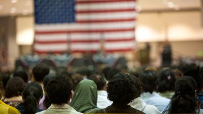 A group of people photographed from behidn facing a large American flag.