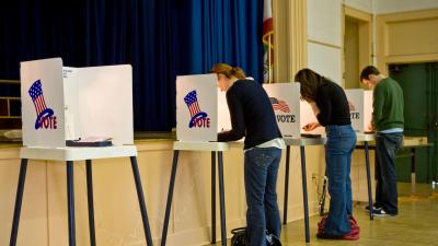 Three people filling out ballots in a row of voting booths