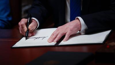 A man's hand signing a piece of paper on a desk