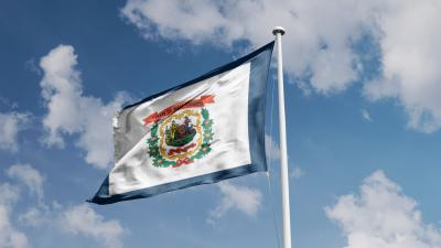 The West Virginia state flag flying against a blue sky with white clouds