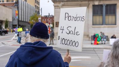 A man holds a sign that says "Pardons 4 Sale $1,000,000."