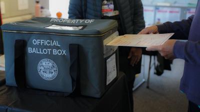 A person inserting a ballot into a box labeled "Official Ballot Box"