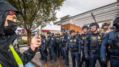 A man wearing a mask films a line of officers with his phone.