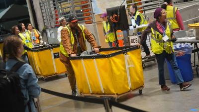 People move large yellow bins full of ballots