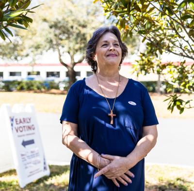 Diane Sherrill Standing under some trees, wearing an 'I Voted' sticker with an 'Early Voting' sign in the background.