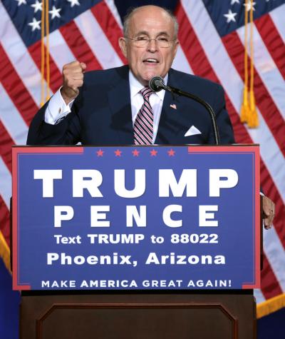 Rudy Giuliani speaking at a podium with a Trump/Pence sign on the front