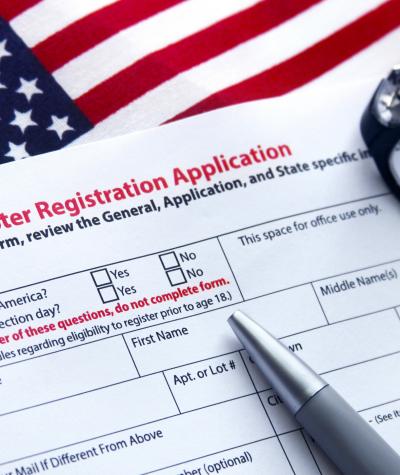 A voter registration form with a pen and glasses on top of an American flag
