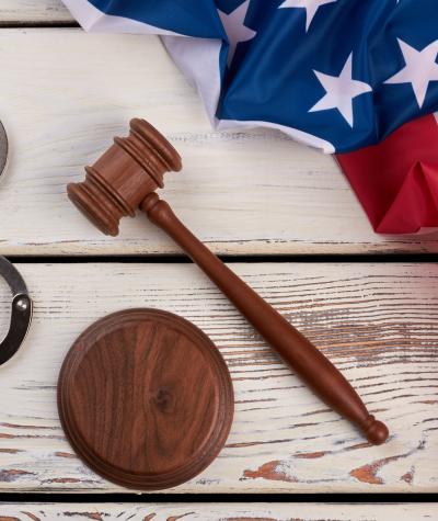 Handcuffs, a gavel and an American flag on a background of white wooden boards