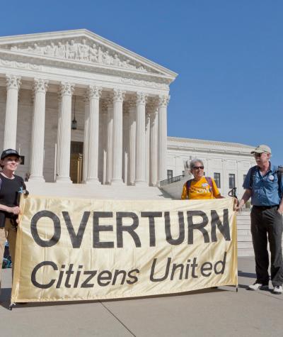 Protesters stand in front of the US Supreme Court holding a sign that says "Overturn Citizens United".