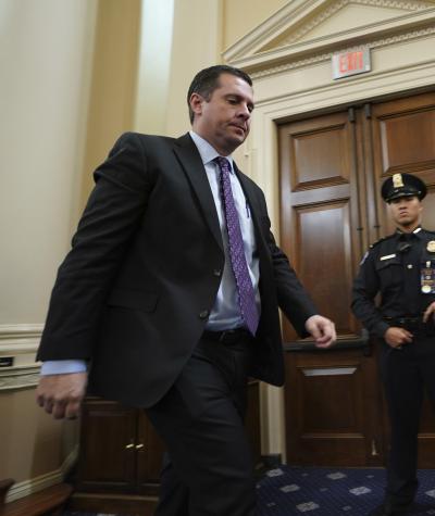 Devin Nunes walking down a hall being photographed by a photographer with a cop in the background