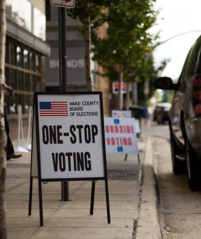 Signs saying "one stop voting" and "curbside voting" along a street with an SUV parked next to them